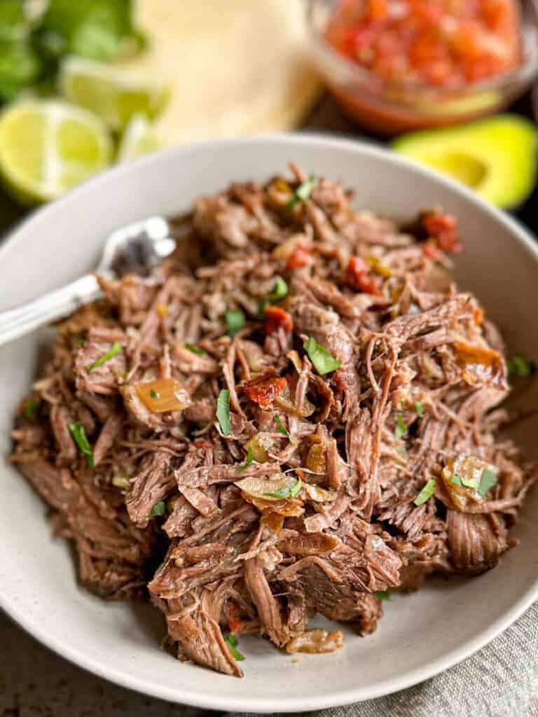 Slow cooker Mexican shredded beef in bowl with cilantro and lime.