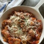 Grilled chicken with bow tie pasta, topped with sauce and cheese.