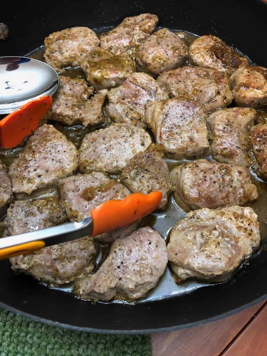 Stove Top Pork Tenderloin Medallions in a pan with chili lime sauce and orange and silver tongs