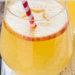 A no stem wine glass filled with apple cider punch, an apple slice and straw.