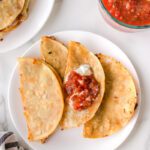 Taco quesadillas on a plate topped with salsa and sour cream.