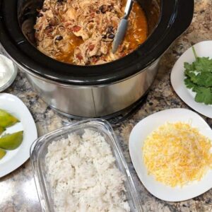 A crockpot full of shredded chicken and taco toppings.