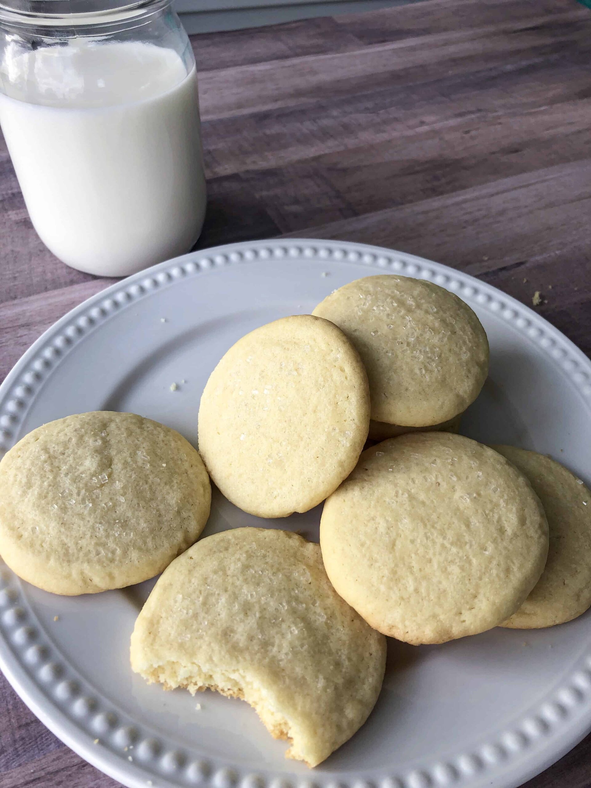 Golden sugar cookies on a plate with a glass of milk.