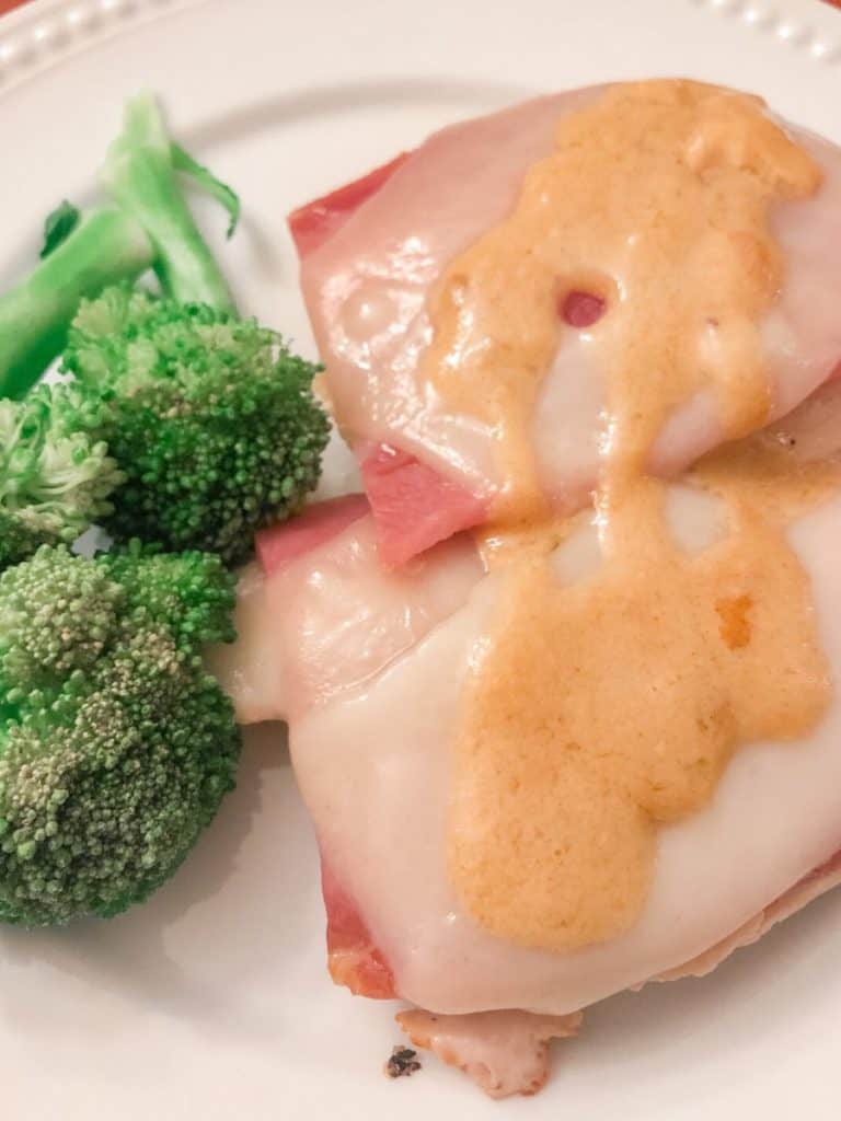 Chicken breasts topped with ham, Swiss cheese and a sauce with broccoli on the side.