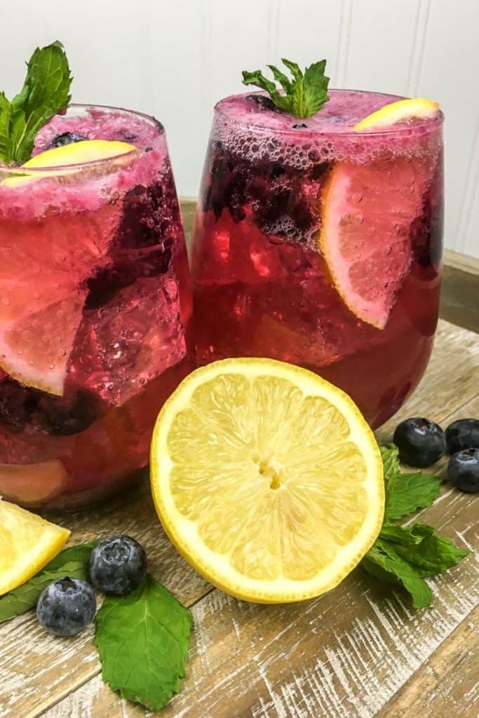 Two glasses filled with blueberry mint lemonade and lemon wedges.