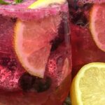 Blueberry mint lemonade in a glass with ice, lemon slice and mint sprig.