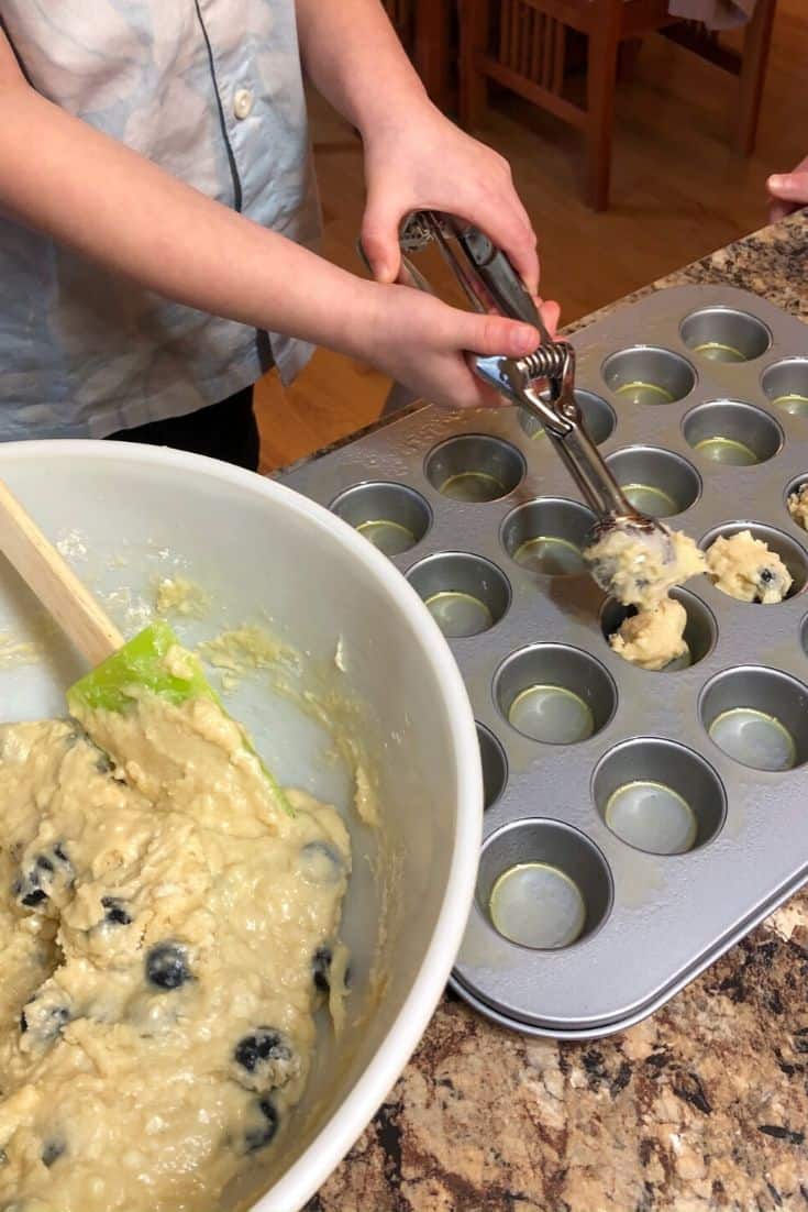 Scooping tablespoons of muffin batter into mini muffin tins to make blueberry muffins.