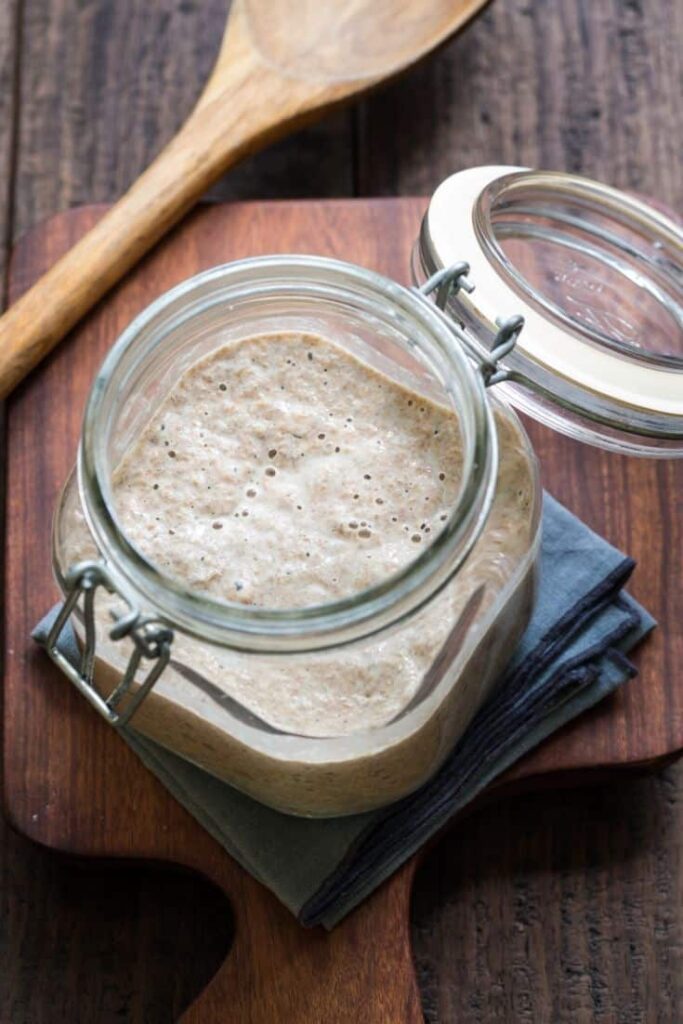 A glass jar of sourdough starter with bubbles on top.