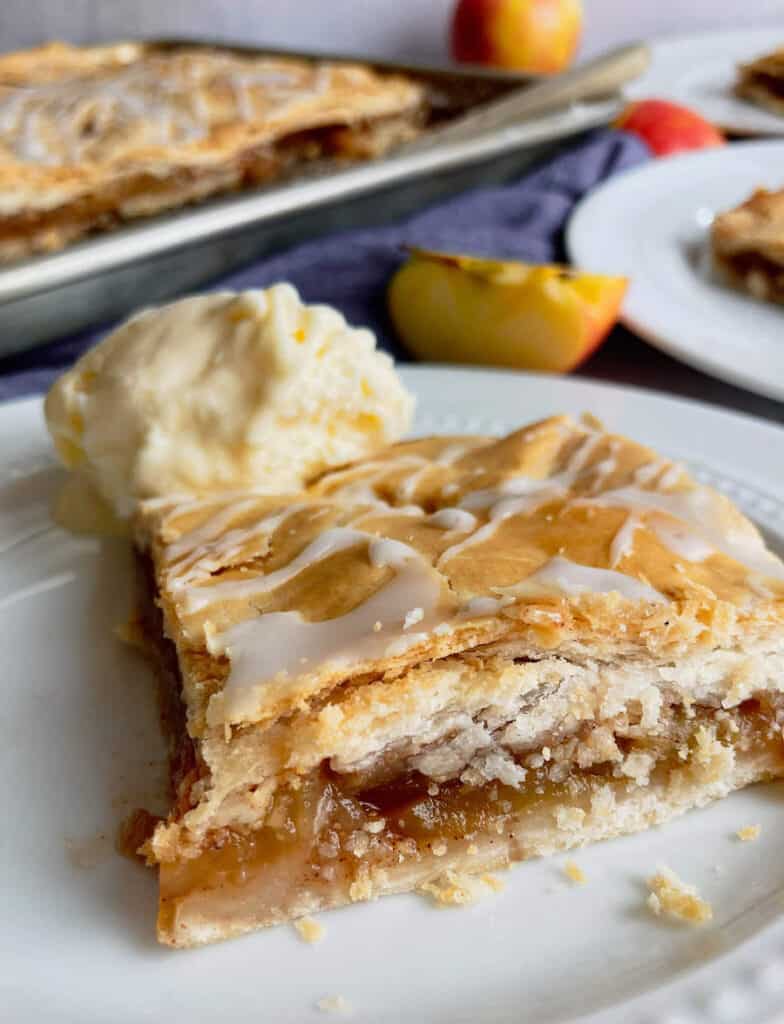 A square of apple pie on a plate with a flaky crust.