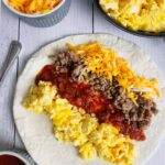 A flour tortilla lined with scrambled eggs, salsa, sausage and cheese.