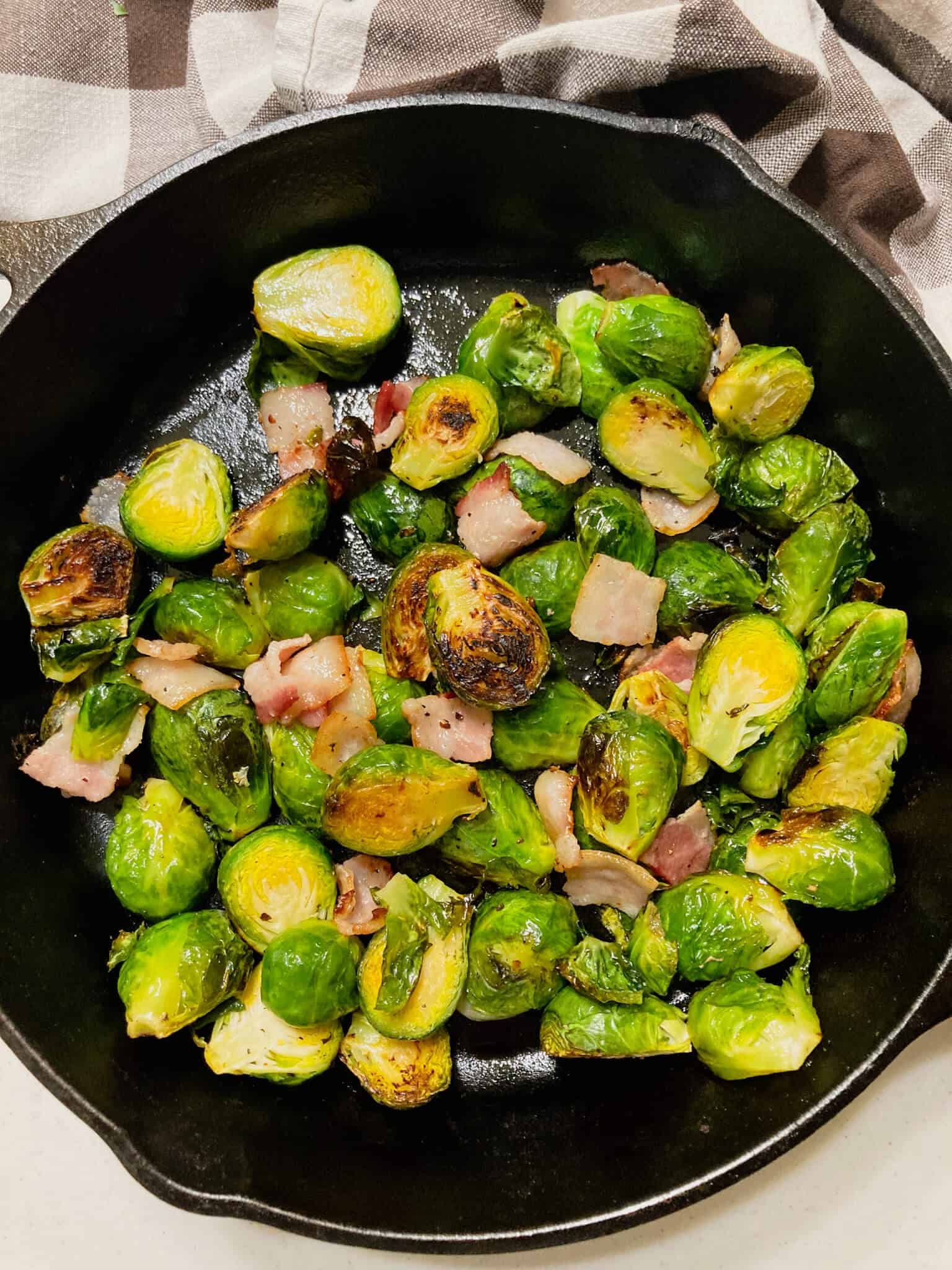 Roasted Brussles sprouts with bacon in a cast iron skillet and buffalo check towel