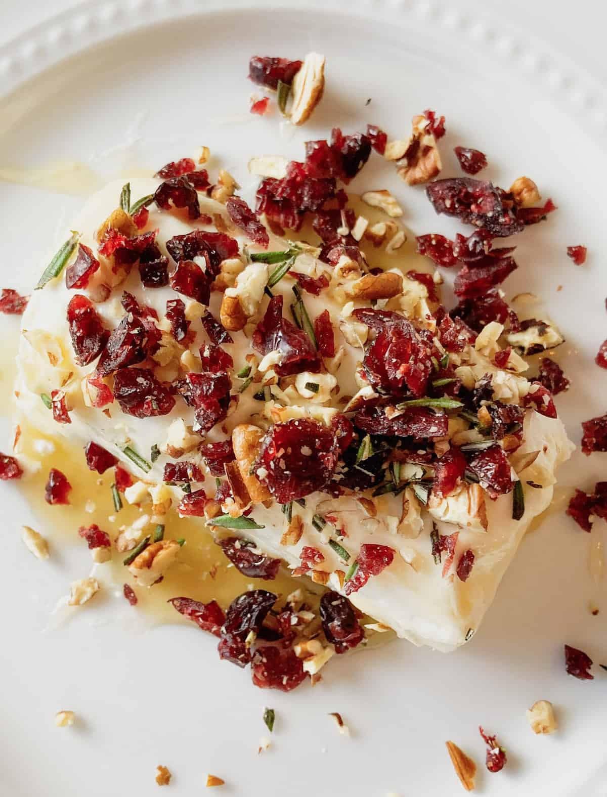 A goat cheese log surrounded by cranberries and pecans on a plate.