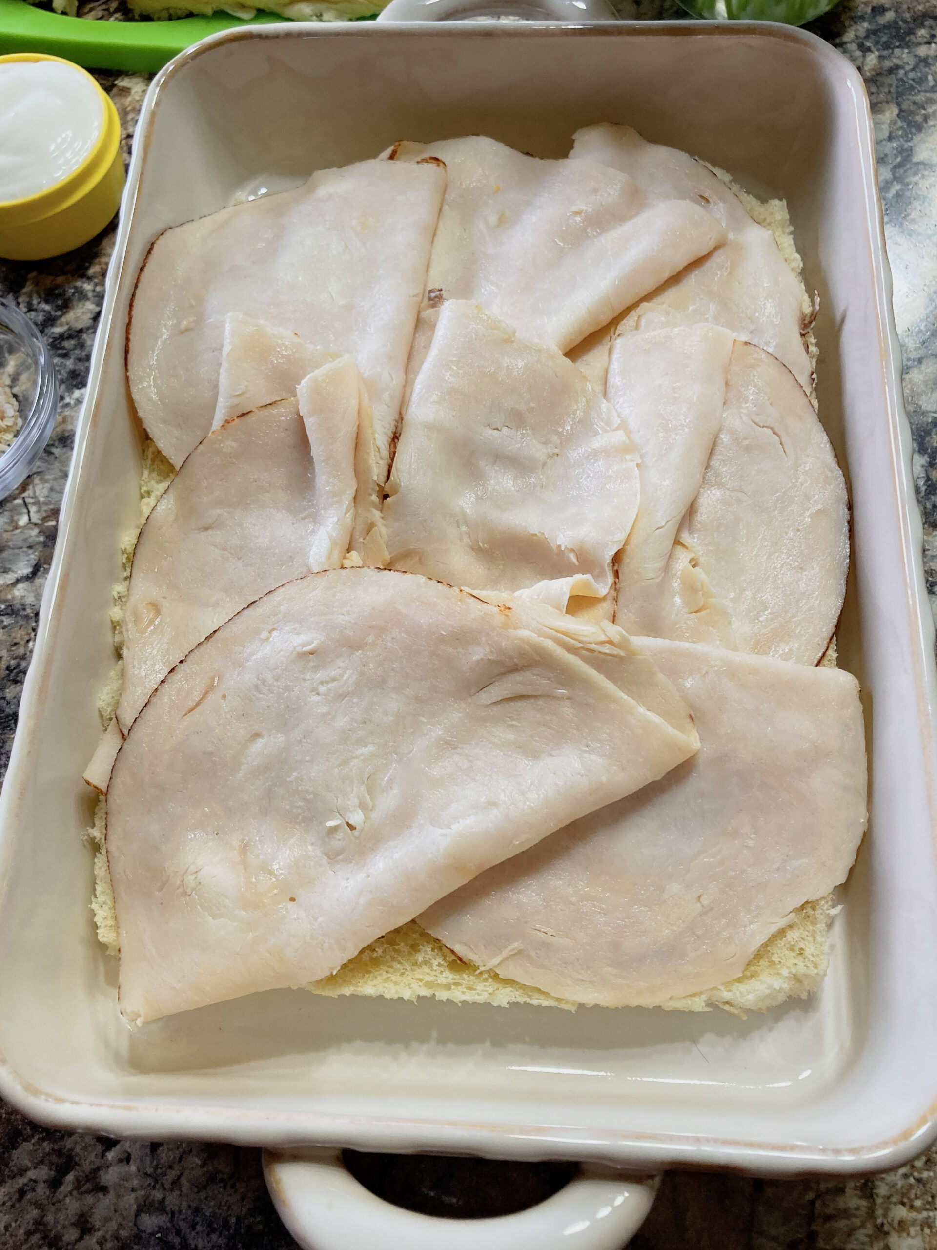 Deli chicken on slider rolls in a casserole dish.