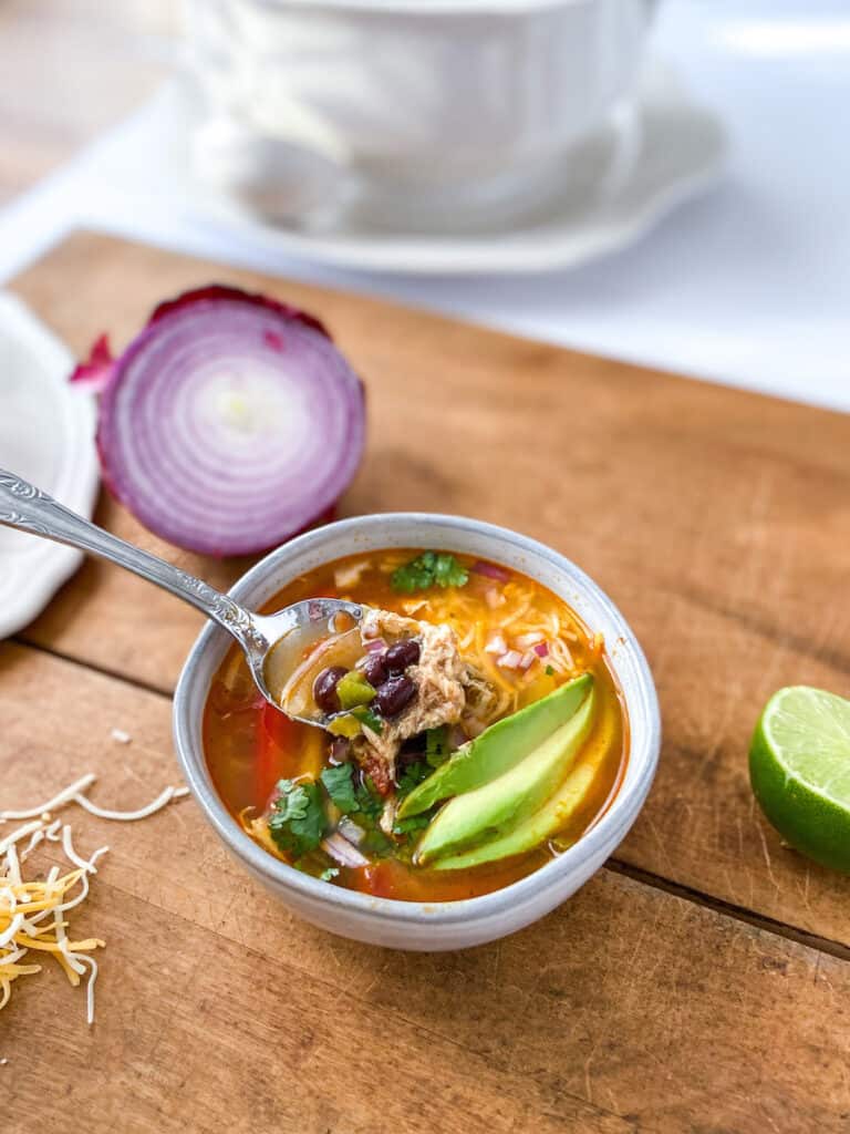 A spoonful of chicken soup with sliced avocado, lime and red onion.