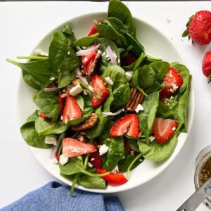 A strawberry spinach salad with feta cheese in a serving bowl.