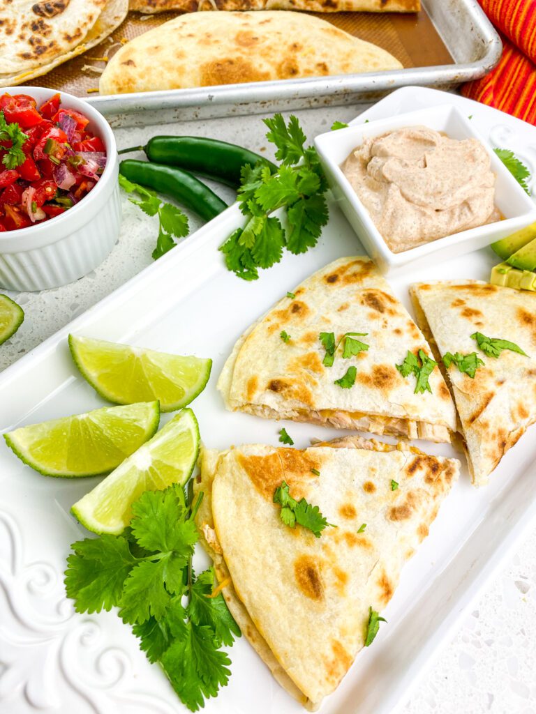 A platter of cheesy chicken quesadillas with salsa and lime wedges.