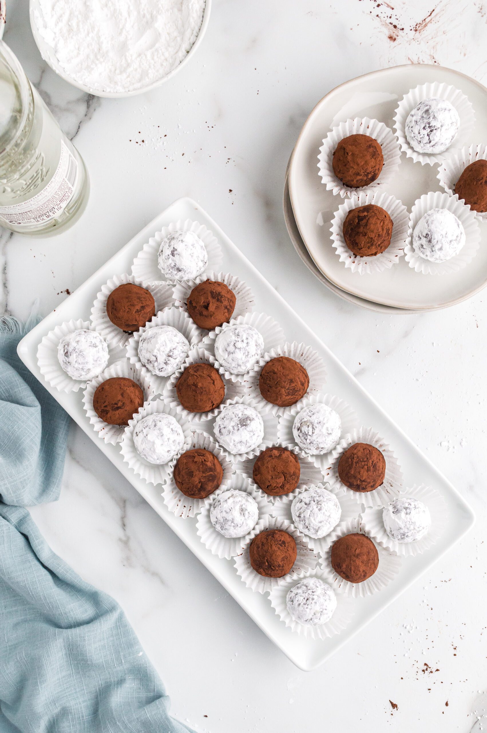 A rectangular platter of coconut rum balls on mini paper wrappers.