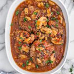 Cooked cube steak with tomatoes and mushrooms in a casserole dish.