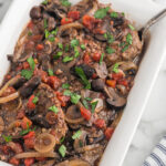 Cooked cube steak with tomatoes and mushrooms in a baking dish.
