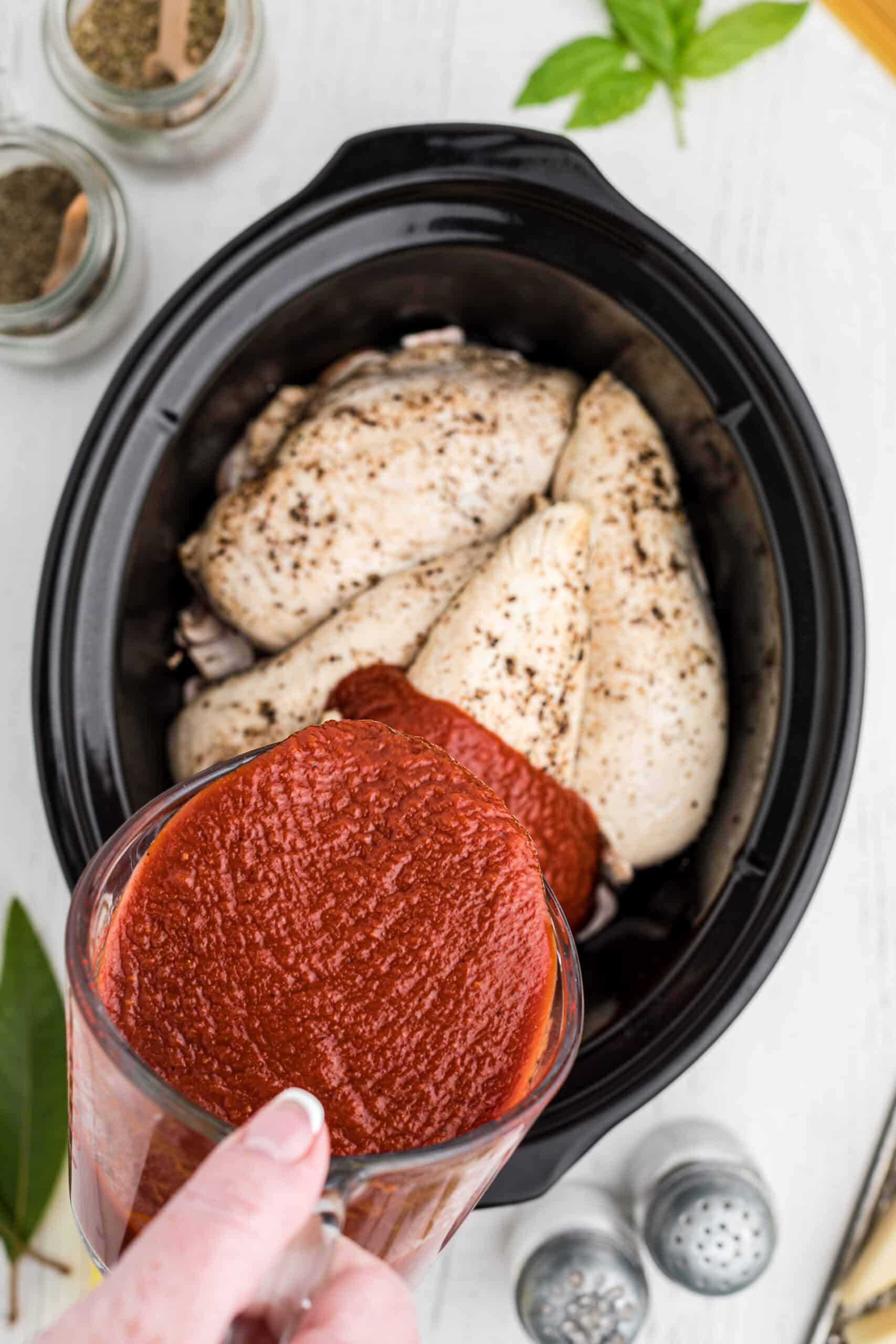Marinara sauce pouring over chicken breasts in the slow cooker.