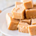 Squares of creamy peanut butter fudge stacked on a plate for sharing.