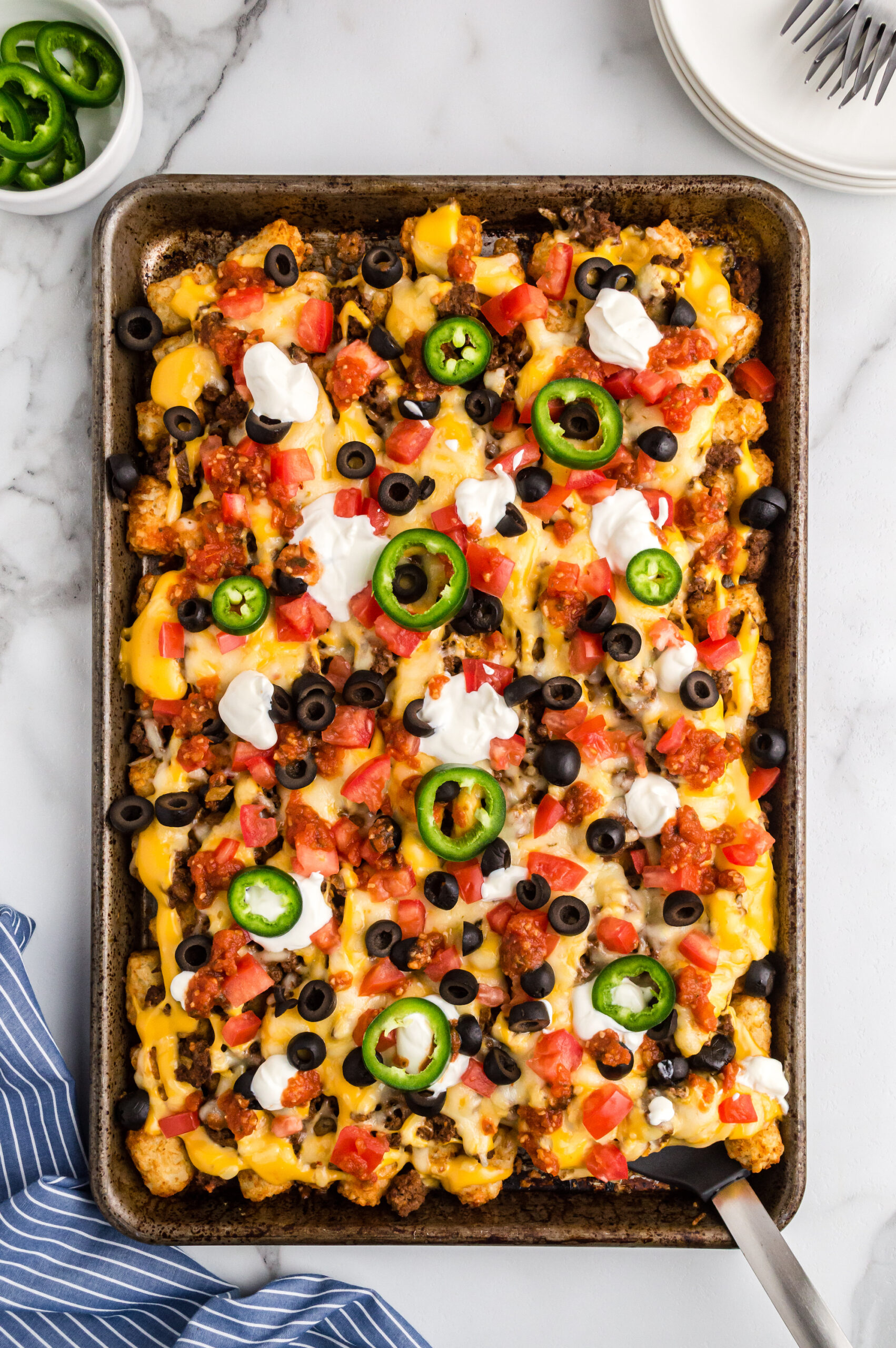 Totchos topped with sour cream, olives, jalapeno slices and cheese.