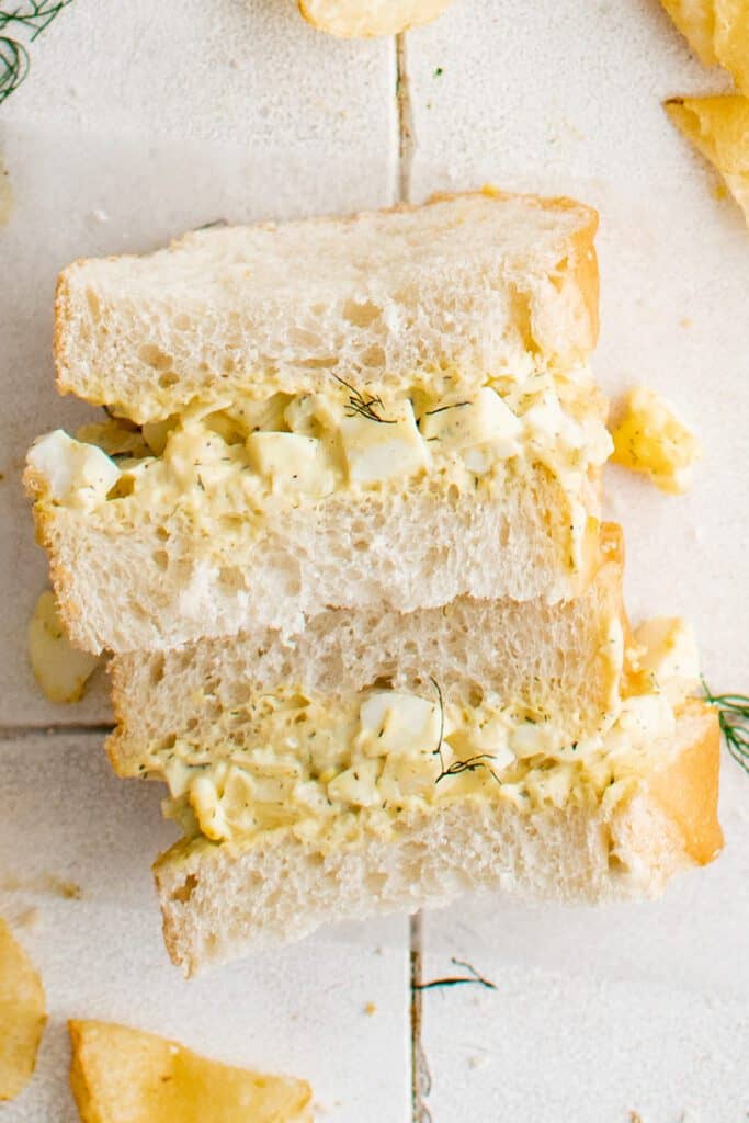 A stack of egg salad sandwiches on white bread sprinkled with fresh dill.