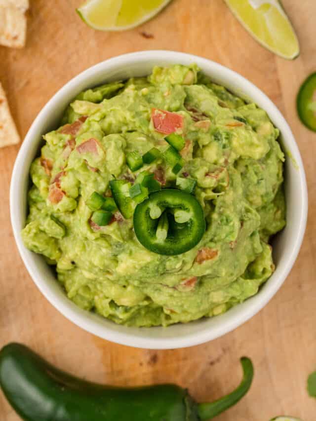 A bowl of mashed avocado guacamole with tomatoes, topped with fresh jalapeno.