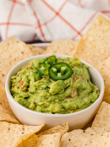 A bowl of guacamole topped with jalapeno slices.