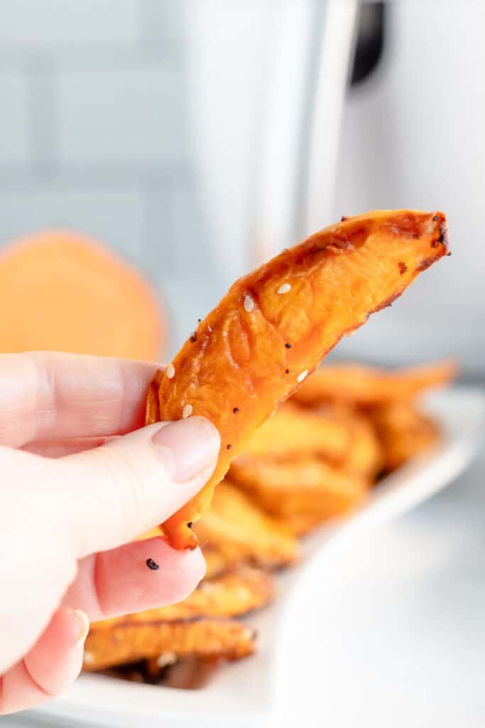 A  hand holding a sweet potato wedge from the air fryer.