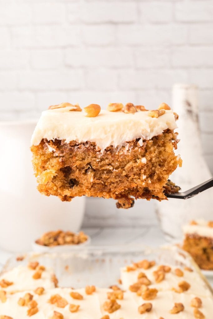 A slice of carrot cake with bits of pineapple topped with a cream cheese frosting.
