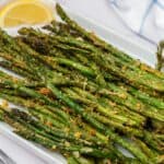 Air fryer asparagus on a platter with lemon wedges.