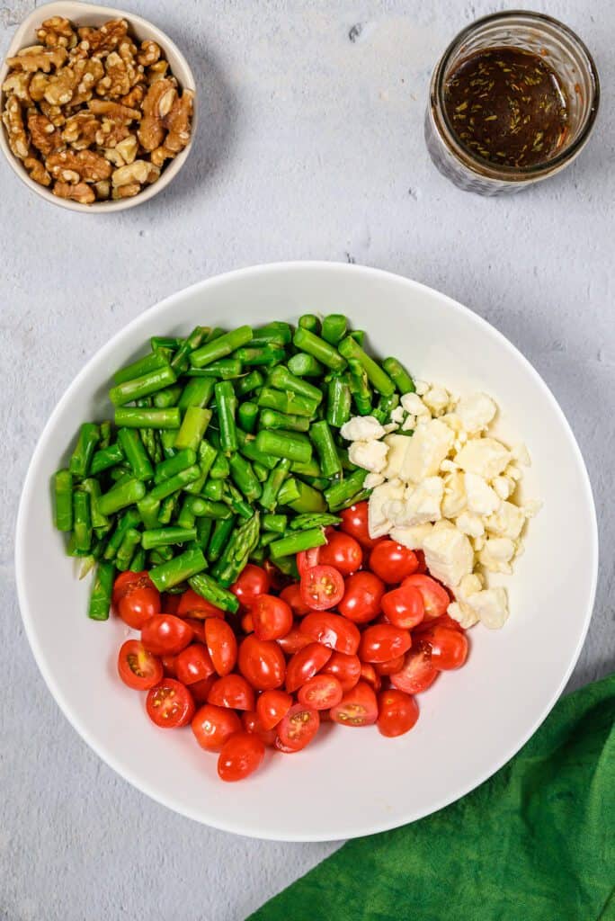 A bowl with sections of chopped asparagus, tomatoes and feta cheese.