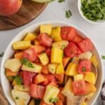 Big bowl of colorful tropical fruit salad featuring pineapple chunks, mango, papaya, and watermelon mixed with lime juice and fresh cilantro.