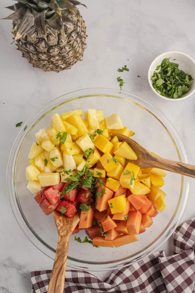 Mexican fruit salad in a glass bowl topped with chopped cilantro.