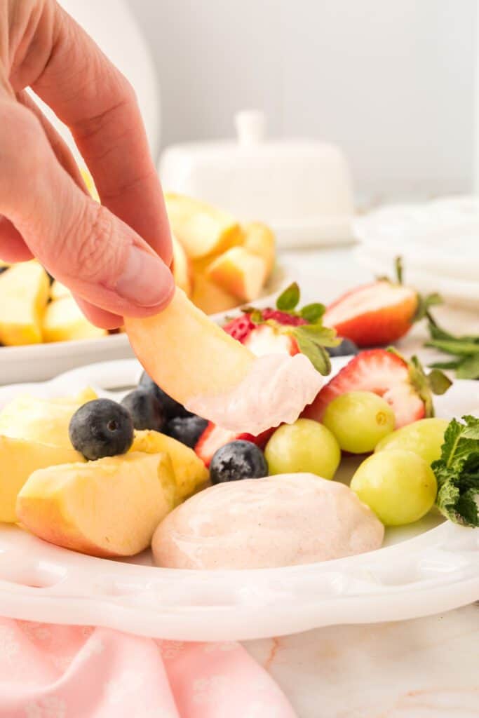 hand dipping yogurt fruit dip from a fruit platter