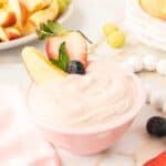 Yogurt fruit dip in a pink bowl with strawberries and apple wedge.