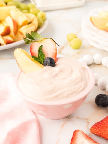 yogurt fruit dip in a pink bowl with strawberries and apple wedge