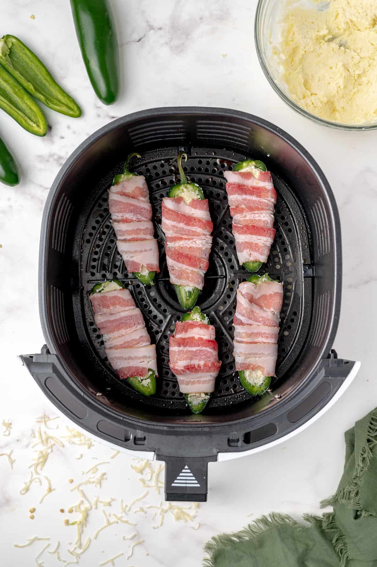 An air fryer basket filled with bacon wrapped jalapeno popper halves.
