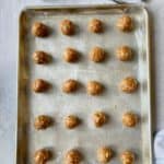 A wax paper covered baking sheet with lines of protein bites and a small scoop.
