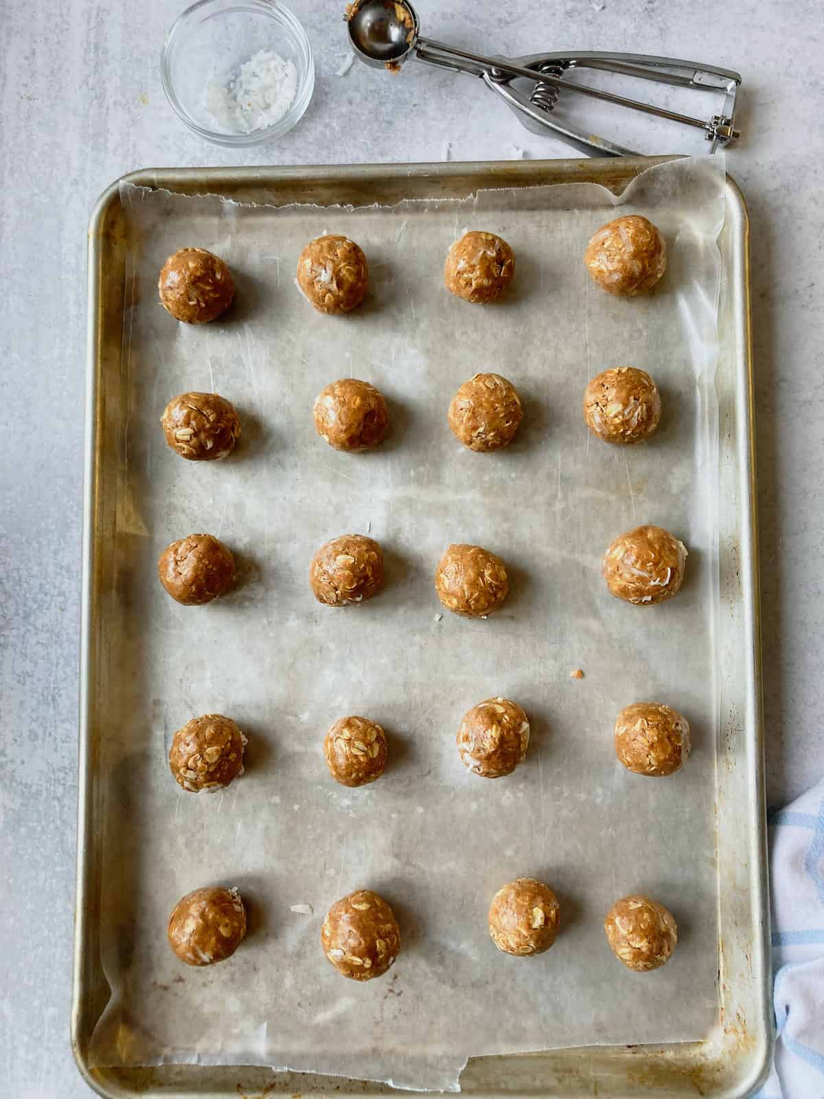 A wax paper covered baking sheet with lines of protein bites and a small scoop.