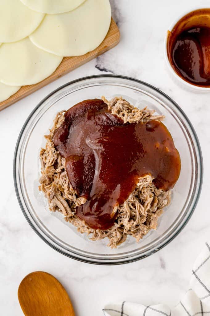 Shredded pork in a large bowl topped with barbecue sauce.