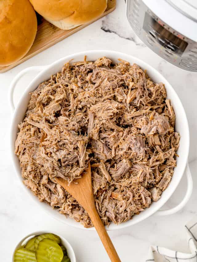 A bowl of pulled pork for serving with a wooden spoon.