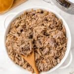 Tender shredded Instant Pot pulled pork made from pork butt, piled high on a sandwich bun with barbecue sauce.