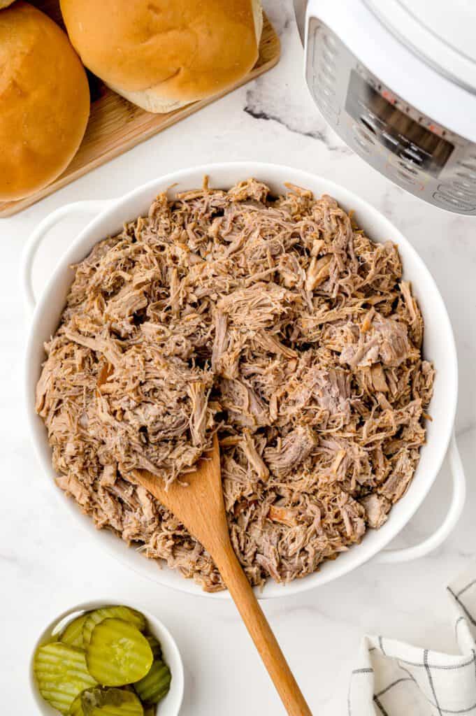 A large bowl of pulled pork with an Instant Pot and sandwich buns.