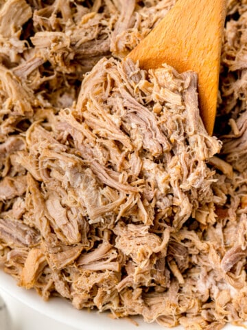 Shredded pulled pork on a large wooden spoon.