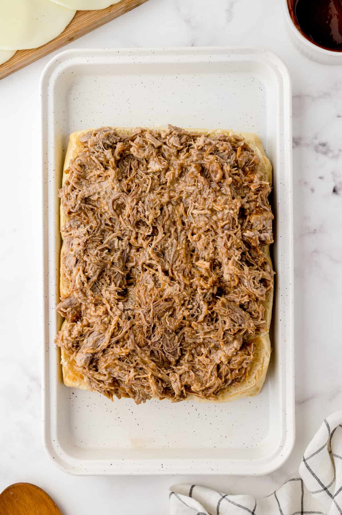 Pulled pork spread on slider buns on a rimmed baking sheet