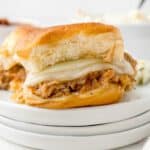 Pulled pork slider on a plate with pickles and coleslaw.
