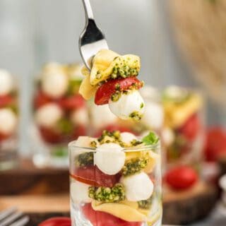 Tortellini, pesto, mozzarella and tomatoes in a small glass cup.