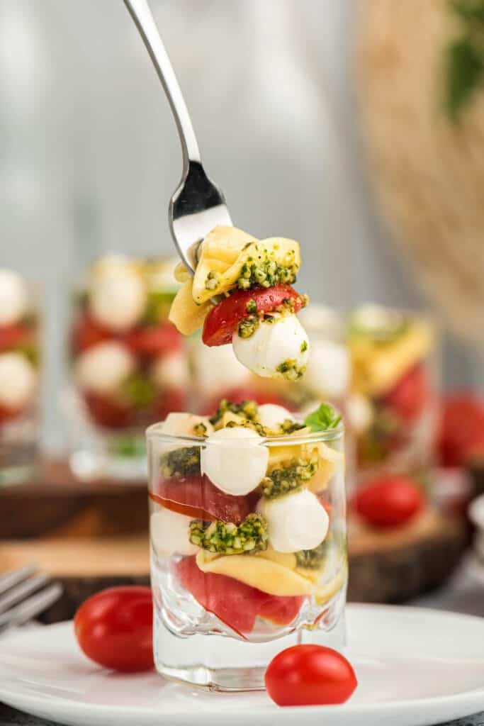 Tortellini, pesto, mozzarella and tomatoes in a small glass cup.